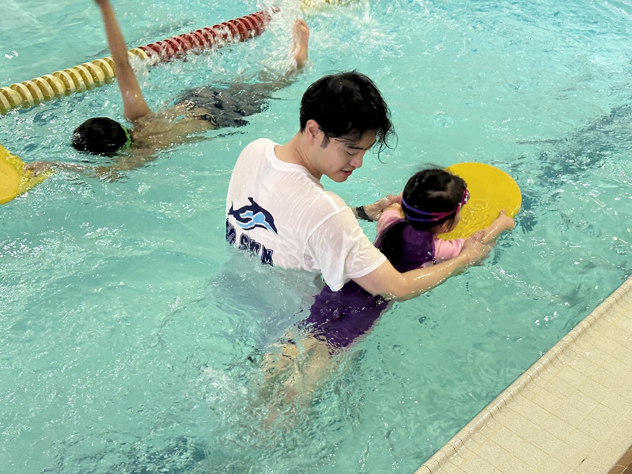 Coach helping a young swimmer with a kickboard at WD Swim North York